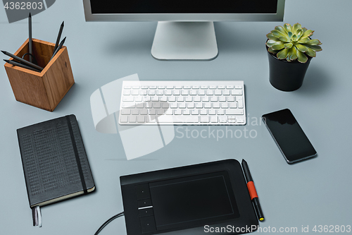 Image of The gray desk with laptop, notepad with blank sheet, pot of flower, stylus and tablet for retouching