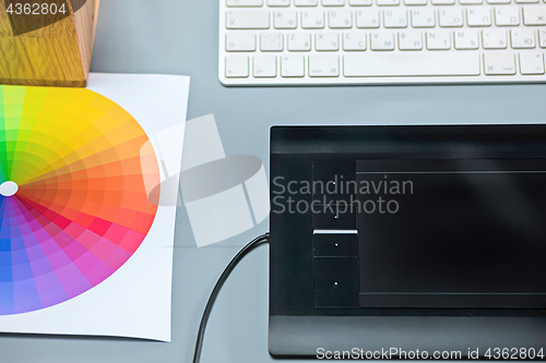 Image of The gray desk with laptop, notepad with blank sheet, pot of flower, stylus and tablet for retouching