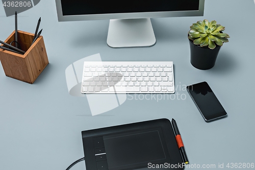 Image of The gray desk with laptop, notepad with blank sheet, pot of flower, stylus and tablet for retouching