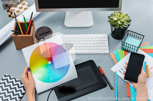 Image of The gray desk with laptop, notepad with blank sheet, pot of flower, stylus and tablet for retouching