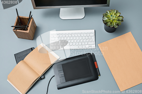 Image of The gray desk with laptop, notepad with blank sheet, pot of flower, stylus and tablet for retouching