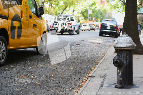 Image of Black fire hydrant on city sidewalk, traffic passing