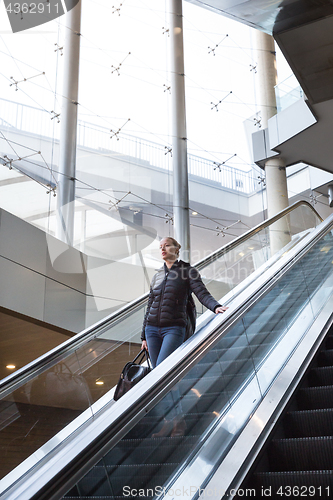 Image of Businesswoman with large black bag and mobile phone descending on escalator.