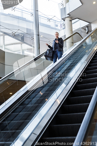 Image of Businesswoman with large black bag and mobile phone descending on escalator.