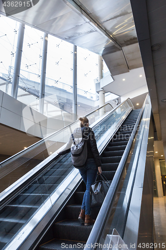 Image of Businesswoman with large black bag and mobile phone ascending on escalator.