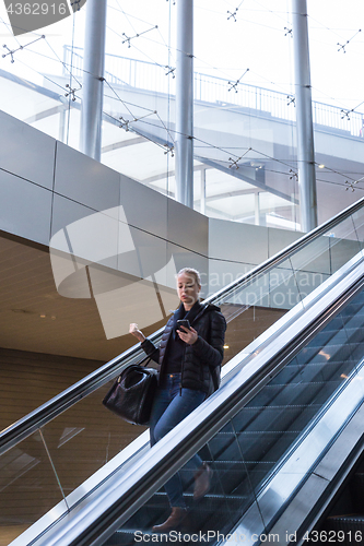 Image of Businesswoman with large black bag and mobile phone descending on escalator.