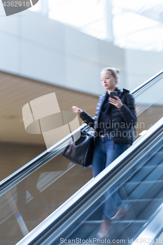 Image of Businesswoman with large black bag and mobile phone descending on escalator.