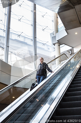 Image of Businesswoman with large black bag and mobile phone descending on escalator.