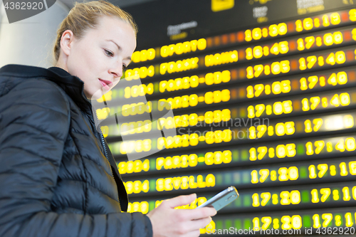 Image of Woman at airport in front of flight information board checking her phone.