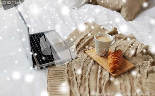 Image of laptop, coffee and croissant on bed at cozy home