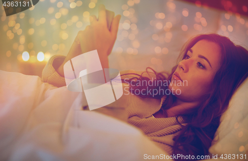 Image of young woman with smartphone in bed at home bedroom