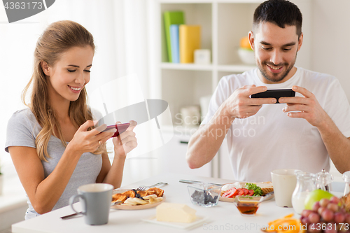 Image of couple with smartphones having breakfast at home