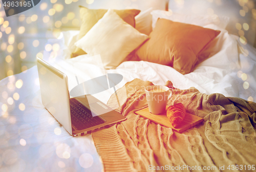 Image of laptop, coffee and croissant on bed at cozy home