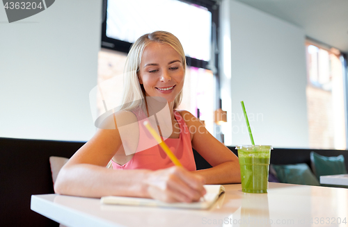 Image of woman with drink writing to notebook at restaurant