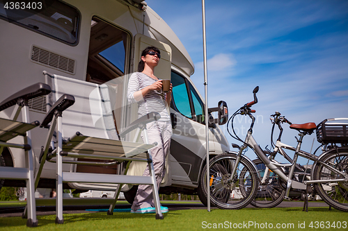 Image of Woman is standing with a mug of coffee near the camper RV.