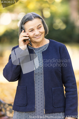 Image of Positive senior woman talking on smartphone outdoors