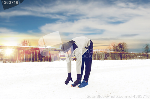 Image of man exercising and stretching leg on winter bridge