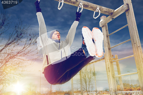 Image of young man exercising on horizontal bar in winter