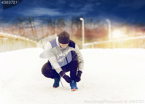 Image of man with earphones tying sports shoe in winter