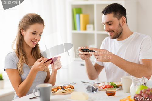 Image of couple with smartphones having breakfast at home