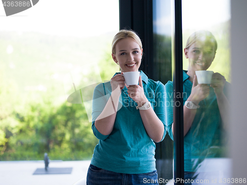 Image of young woman drinking morning coffee by the window