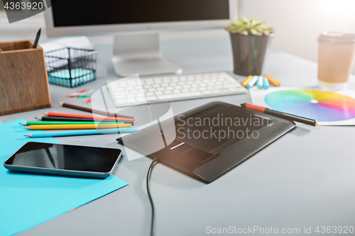 Image of The gray desk with laptop, notepad with blank sheet, pot of flower, stylus and tablet for retouching