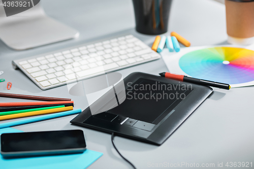 Image of The gray desk with laptop, notepad with blank sheet, pot of flower, stylus and tablet for retouching