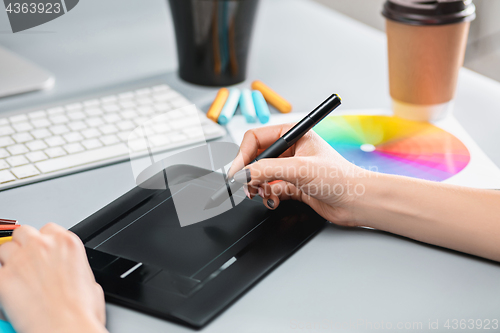 Image of The gray desk with laptop, notepad with blank sheet, pot of flower, stylus and tablet for retouching