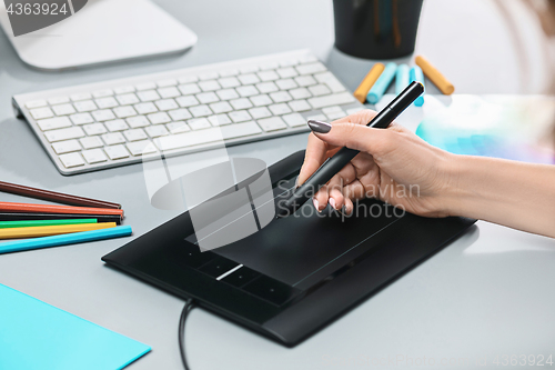 Image of The gray desk with laptop, notepad with blank sheet, pot of flower, stylus and tablet for retouching