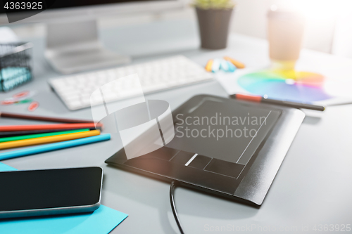 Image of The gray desk with laptop, notepad with blank sheet, pot of flower, stylus and tablet for retouching