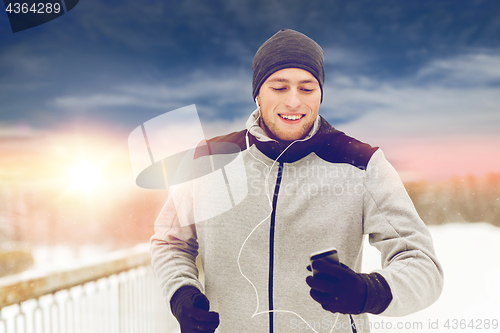 Image of happy man with earphones and smartphone in winter