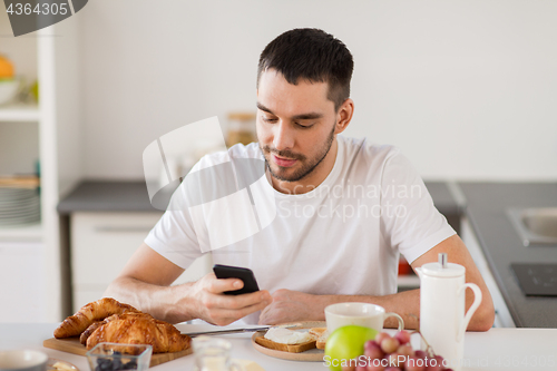 Image of man with smartphone having breakfast at home