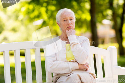 Image of sad senior woman sitting on bench at summer park