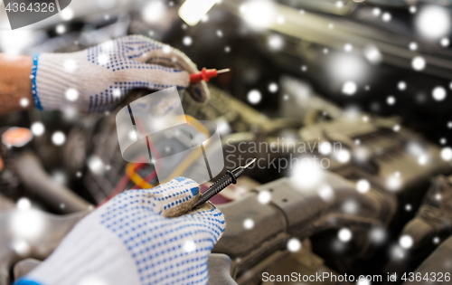 Image of auto mechanic hands with multimeter at car