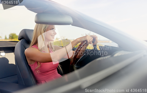 Image of happy young woman driving convertible car