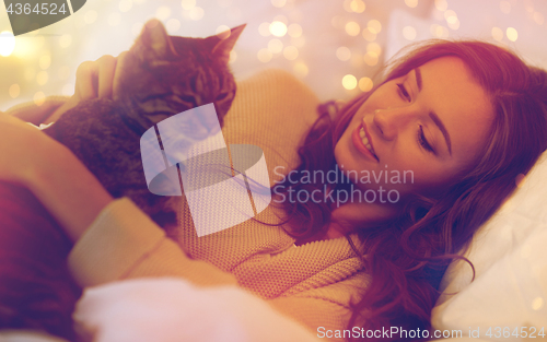 Image of happy young woman with cat lying in bed at home