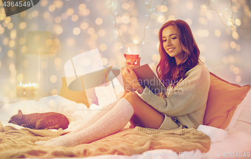 Image of happy young woman reading book in bed at home