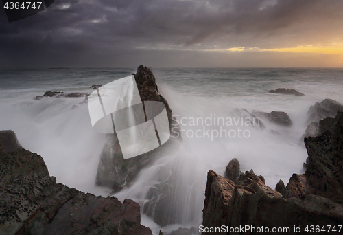 Image of Stormy sunrise and waves crash over sea stacks