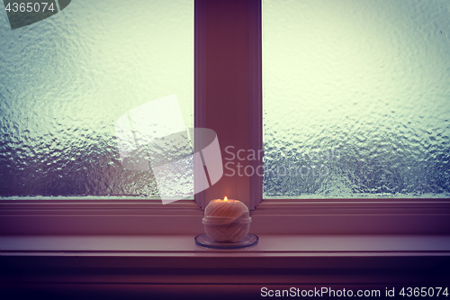Image of Burning candle and frosted window in winter twilight