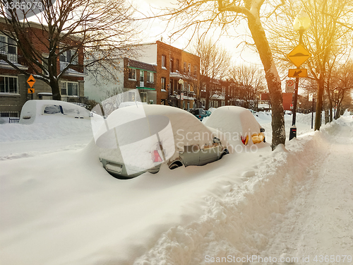 Image of Cars covered with snow on winter street in sunset