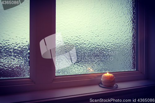 Image of Candle burning near a frosted window in twilight