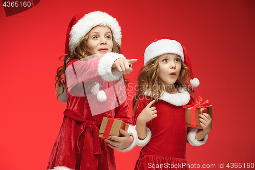 Image of Two happy girls in santa claus hats with gift boxes