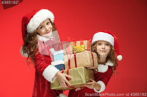 Image of Two happy girls in santa claus hats with gift boxes