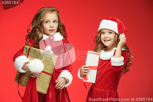 Image of Two happy girls in santa claus hats with gift boxes