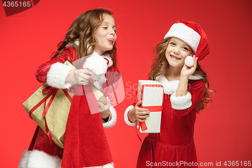 Image of Two happy girls in santa claus hats with gift boxes