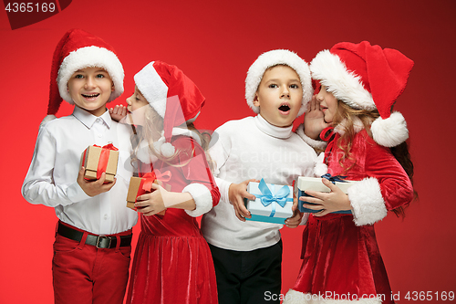 Image of Two happy girls and boys in santa claus hats with gift boxes