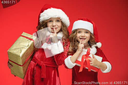 Image of Two happy girls in santa claus hats with gift boxes