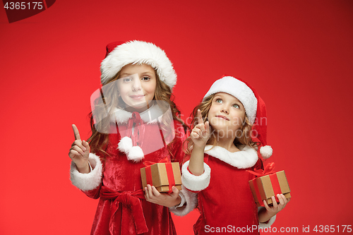 Image of Two happy girls in santa claus hats with gift boxes