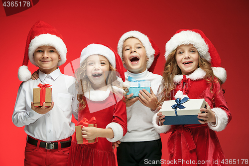 Image of Two happy girls and boys in santa claus hats with gift boxes