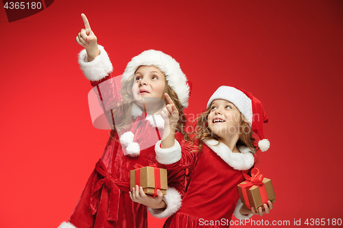 Image of Two happy girls in santa claus hats with gift boxes